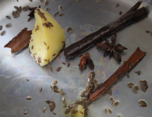 Image of a cinnamon stick, some cloves, and star anise frying in oil.